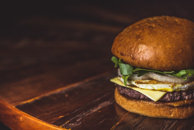 A burger with a patty, cheese, onions, and lettuce between halves of a bun placed on a wooden table.